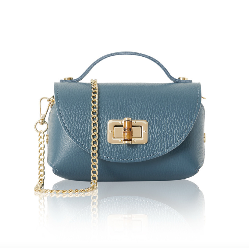 A small, structured denim blue leather handbag with a textured finish, featuring a gold turn-lock closure on the front flap, a short top handle, and a detachable gold chain shoulder strap. 